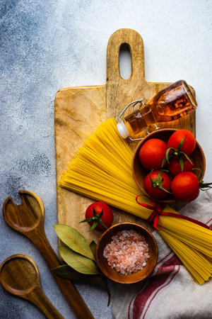 Pasta cooking concept with raw spaghetti and tomato on rustic backgroundの写真素材