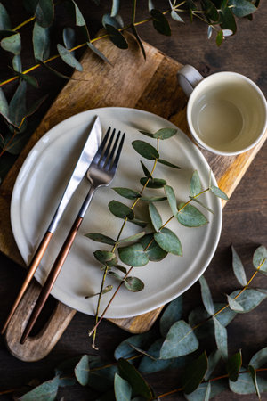Place setting with fresh eucalyptus leaves on wooden tableの写真素材