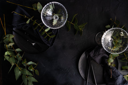 Dark stoneware with black cutlery served on black concrete background decorated with fresh green...