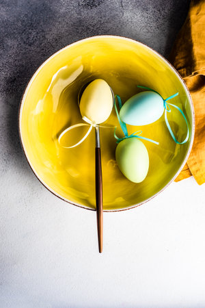 Bright yellow bowl decorated with colored eggs on concrete background