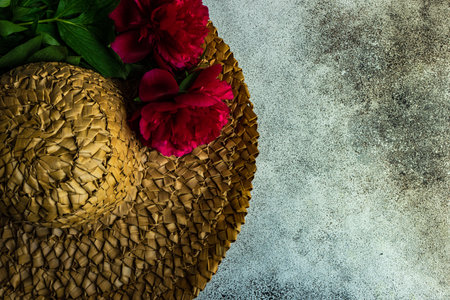 Summer background with straw har decorated with bright red peony flowers on concrete backgroundの写真素材