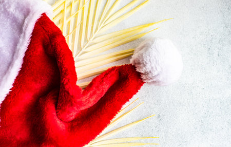 Christmas card concept with palm leaves and Santa hat on white sand backgroundの写真素材