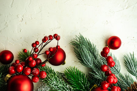 Christmas card concept with frame made with green fir branches, red decoration balls and berries on concrete backgroundの写真素材