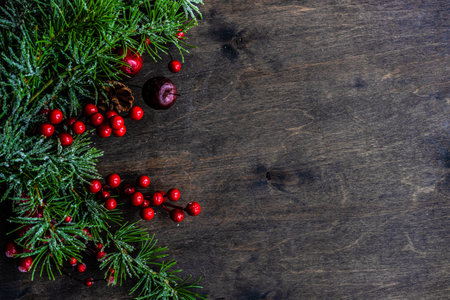 Christmas card concept with frame made with green fir branches, red decoration balls and berries on concrete background
