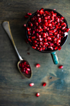 Ripe organic pomegranate fruit on the ceramic cup and vintage spoon on wooden tableの写真素材