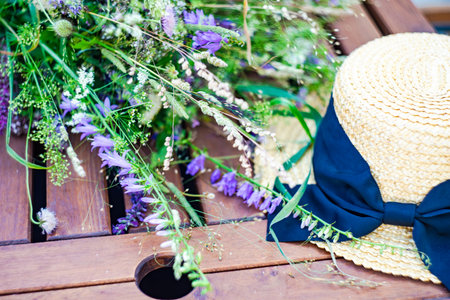Beautiful wild flowers in bouquet and straw hat on wooden tableの写真素材