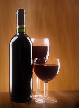 Red wine glass and bottle on a wooden background. Low key, still life.の写真素材