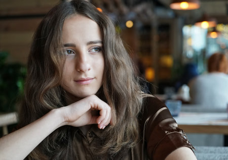 She looks out the window, lost in thought. Dark curly hair, mouth closed, natural make-up and skin.の写真素材