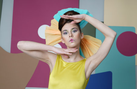 Eccentric outfit: short dress with open shoulders, headdress made of paper, fingers under her chin and over head. Color background: circles, rectanglesの写真素材