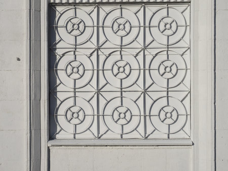 White facade of the house with a wrought iron grating on the window. Simple geometric shapes on the grid: circles, lines. Beautiful shadow game on white background. Concept: white on the whiteの写真素材