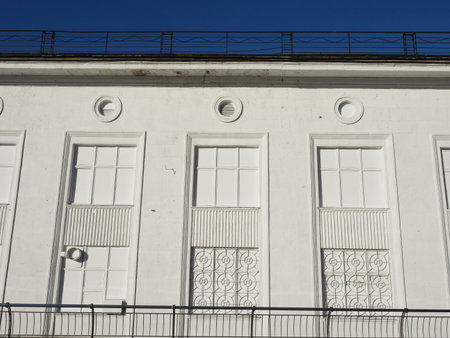 White facade of the house with a wrought iron grating on a series of imaginary windows. Simple geometric figures: circles, lines, squares against the blue sky. Concept: white on the whiteの写真素材