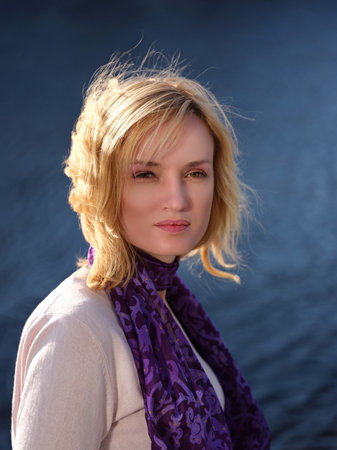 A shoulder portrait of a beautiful young blonde. She looks at the camera. She is dressed in a light sweater, on her neck a shawl.の写真素材