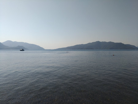 Beatiful sea summer panorama.  Beach scene at Pukka region, yachts, boats, mountains, shot at Marmaris, Turkey. blue sky, tourists in swimsuits, umbrellas, people resting, swimmingの写真素材