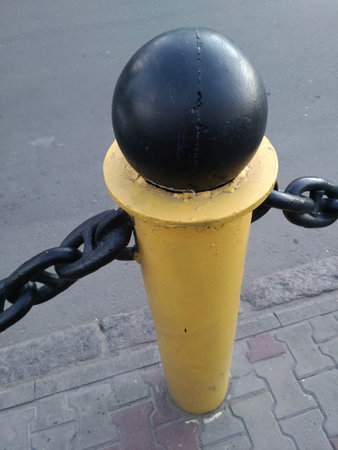 Stylus of street fencing made of metal with chain. The design of the fence is a yellow tube support, hinges, a black metal ball on top. Stylistics of the seaportの写真素材