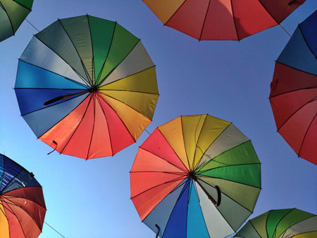 Multicolored umbrellas against the sky in the backlight. Decorative canopy, red, blue green, yellow. Colors of rainbow. The art of street decor, the atmosphere of a holiday, summer, rest, rain is not a hindranceの写真素材