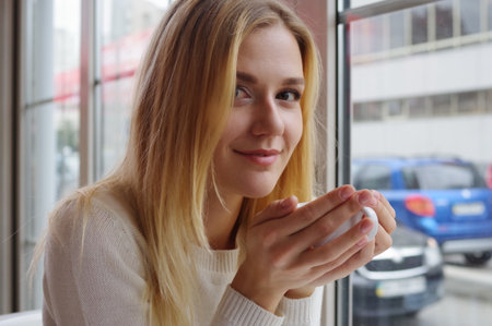 Portrait of a blonde in a white sweater, warming hands with a cup of tea.の写真素材