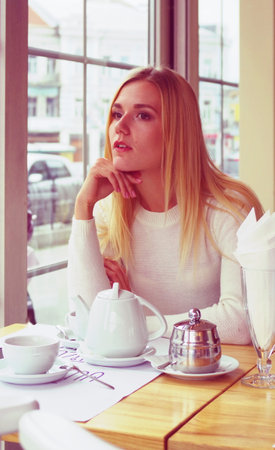 Beautiful young woman is thinking about her ideas in a cafe. With a teapot and sparkling water on her table.の写真素材