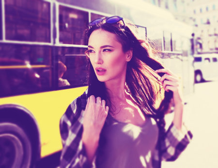 Street portrait of a beautiful brunette woman in a plaid shirt. Sunglasses on the head. Reflection of the sky in glasses glasses. Inviting look of a young woman. Mysterious smile.の写真素材