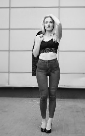 Sexy pretty girl is posing on a street. Wearing blue jeans and black crop top. Her leather coat is in her right hand on the shoulder.の写真素材