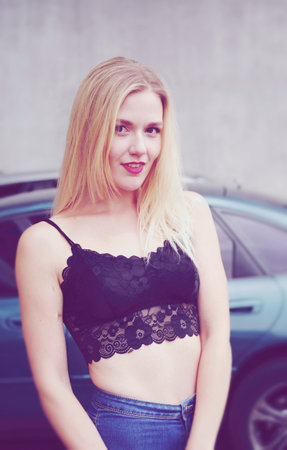 Sexy girl is posing in a car park. Wearing blue jeans and black crop top. She is smiling. With good long blonde hair.の写真素材