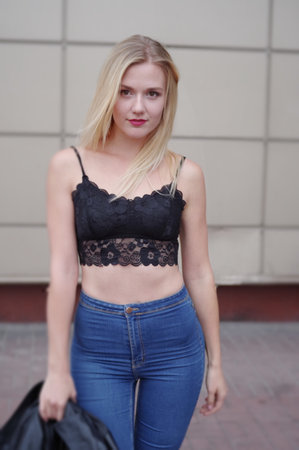 Pretty girl is posing on a street. Wearing blue jeans and black crop top. She has good long blonde hair. Wall on the background.の写真素材