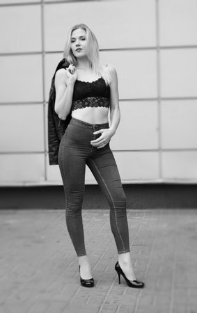 Beautiful girl is posing on a street. Wearing blue jeans and black crop top. Her leather coat is in her right hand on the shoulder.の写真素材