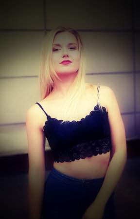 Beautiful girl is posing on a street. Wearing blue jeans and black crop top. She has good long blonde hair. Wall on the background.の写真素材