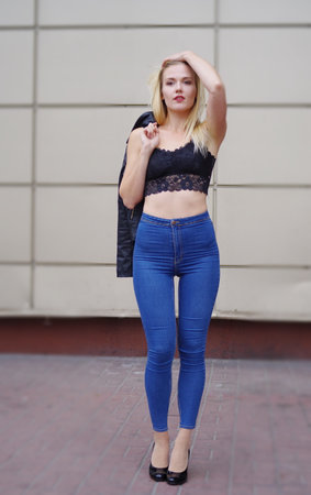 Sexy pretty girl is posing on a street. Wearing blue jeans and black crop top. Her leather coat is in her right hand on the shoulder.の写真素材
