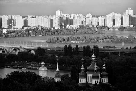 KYIV - UKRAINE. Sunset cityscape in Kyiv over the Dnipro river. With an orthodox church with golden domes, bridge, river itself and build-up area on another bank. There are many green trees.の写真素材