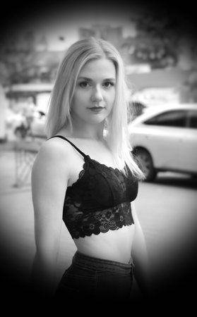 Pretty female is posing on a street. Wearing blue jeans and black crop top. Near a shopping mall. Cars on the background.の写真素材