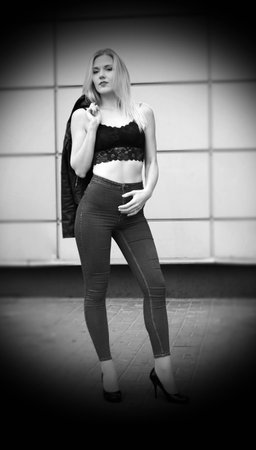 Beautiful girl is posing on a street. Wearing blue jeans and black crop top. Her leather coat is in her right hand on the shoulder.の写真素材