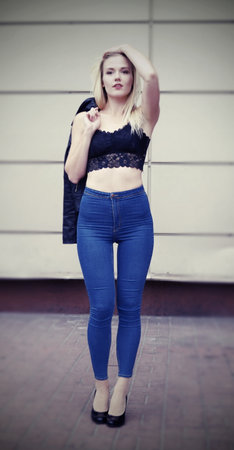 Sexy pretty girl is posing on a street. Wearing blue jeans and black crop top. Her leather coat is in her right hand on the shoulder.の写真素材
