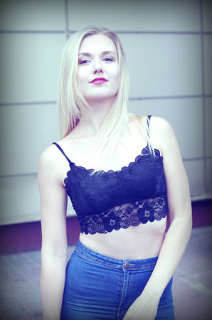 Beautiful girl is posing on a street. Wearing blue jeans and black crop top. She has good long blonde hair. Wall on the background.の写真素材