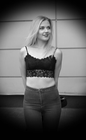 Flirting girl is posing on a street. Wearing blue jeans and black crop top. She has good long blonde hair. Wall on the background.の写真素材
