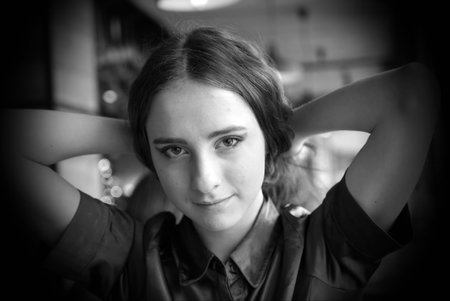 Portrait of a young girl in a brown blouse in a cafe. A beautiful girl is sitting in a cafe holding hands behind her head. Big brown eyes, curly hair, natural make-up.の写真素材