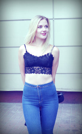 Flirting girl is posing on a street. Wearing blue jeans and black crop top. She has good long blonde hair. Wall on the background.の写真素材