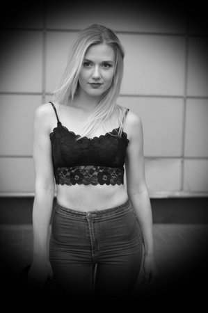 Pretty girl is posing on a street. Wearing blue jeans and black crop top. She has good long blonde hair. Wall on the background.の写真素材