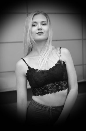 Beautiful girl is posing on a street. Wearing blue jeans and black crop top. She has good long blonde hair. Wall on the background.の写真素材