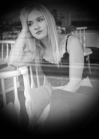 Portrait of a blonde beautiful girl in a playful pose. She is wearing a lacy tops crochet and jeans. The street fashion. The picture is taken through the window of a street cafe.の写真素材