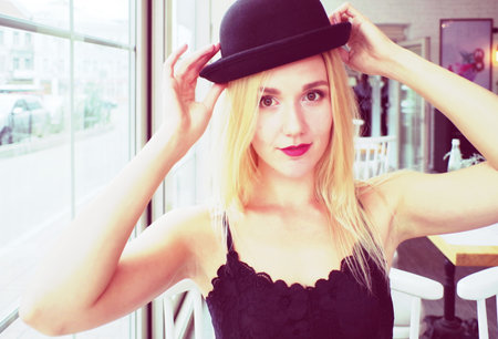 Sexual portrait of a blond beautiful woman  in a black lace crop top, jeans and a black hat. An outdoor cafe.の写真素材