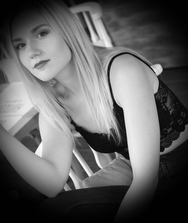 Portrait of a blonde girl in a black lace crocheted top and jeans, sitting in a playful pose on the couch. Fashion, street style.の写真素材