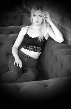 Portrait of a blonde girl in a black lace crocheted top and jeans, sitting in a playful pose on the couch.の写真素材