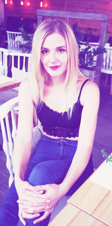 Portrait of a blonde girl in a black lace crocheted top and jeans, sitting in a playful pose on the couch. Fashion, street style.の写真素材