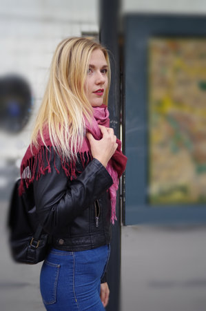 Cold. A beautiful blonde girl is standing at a public transport stop. The girl is dressed in a black jacket and jeans with a high waist. Street style.の写真素材