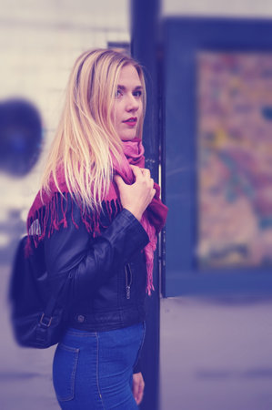 Cold. A beautiful blonde girl is standing at a public transport stop. The girl is dressed in a black jacket and jeans with a high waist. Street style.の写真素材
