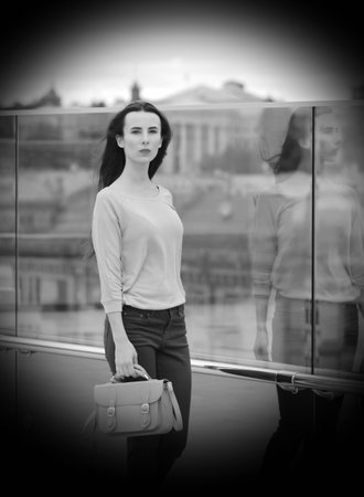 Pretty young woman posing near a glass wall in the downtown. She is wearing burgundy jeans, pink shirt and yellow shoes, with yellow handbag in her right hand.の写真素材