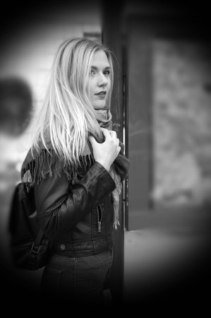 Cold. A beautiful blonde girl is standing at a public transport stop. The girl is dressed in a black jacket and jeans with a high waist. Street style.の写真素材