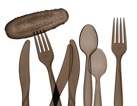 Dark silhouettes on a white background with different kitchenware: forks, spoons and knives. A cucumber is on a fork. All items are made of plastic and are transparent.の写真素材