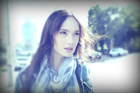 Young woman posing while walking around the city in windy weather. She wears a blue jeans jacket with a scarf.の写真素材