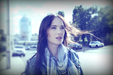 Young woman posing while walking around the city in windy weather. She wears a blue jeans jacket with a scarf.の写真素材